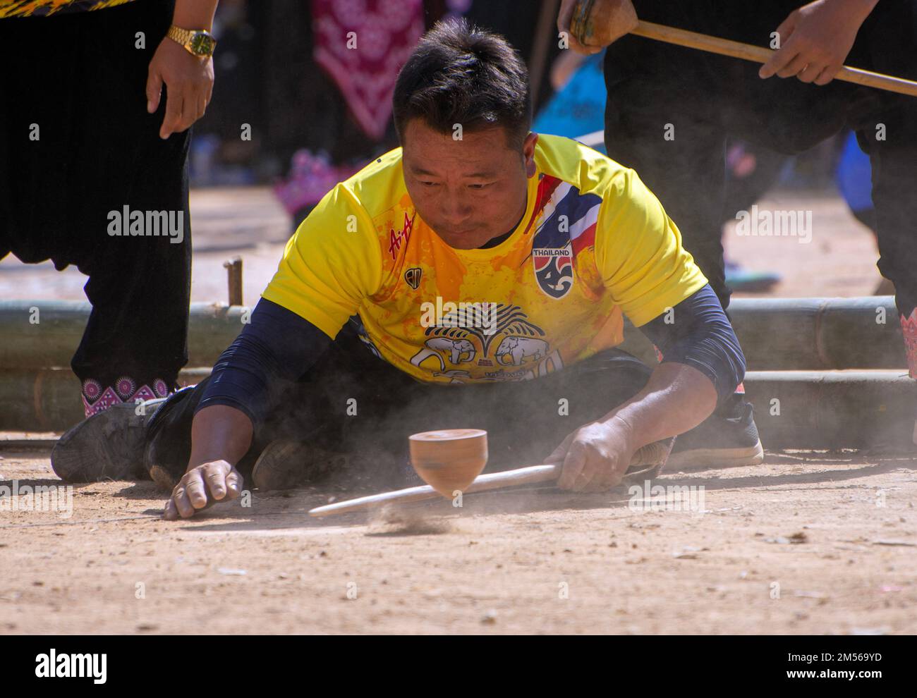 Un homme de tribu de colline de Hmong jouant à la compétition de rotation de haut (jeu traditionnel de tujlub qui implique la rotation de hauts en bois hurlé avec des cordes et des bâtons. Alors qu'un sommet tourne encore, une autre personne essaie du frapper. S'ils ne le frappent pas, ils sont sortis. S'ils le frappent, le gagnant est celui dont le haut continue à tourner le plus longtemps.) Pendant les célébrations du nouvel an de Hmong. En décembre ou janvier, les Hmong célèbrent leur nouvelle année, appelée Noj PEB Caug (prononcé ou PE Chao). Une plus grande célébration publique a lieu dans un lieu en plein air, il y a de nombreuses activités pendant cet événement, comme les TOP-s. Banque D'Images