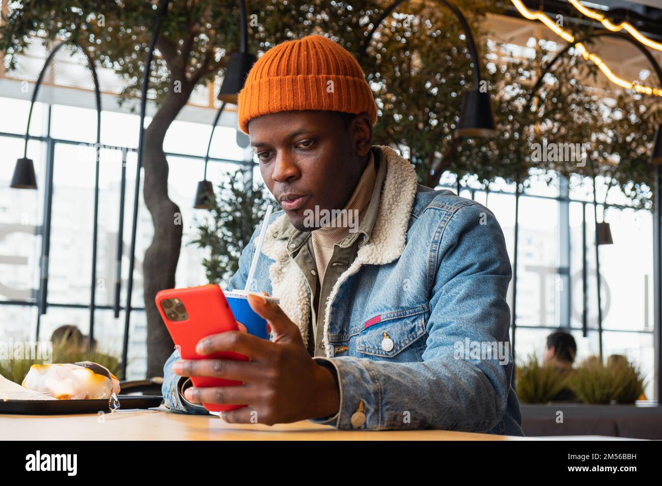 Joli homme noir en bonnet tricoté orange et veste en denim utilise un  smartphone moderne assis à table dans un café décoré de gros plan Photo  Stock - Alamy