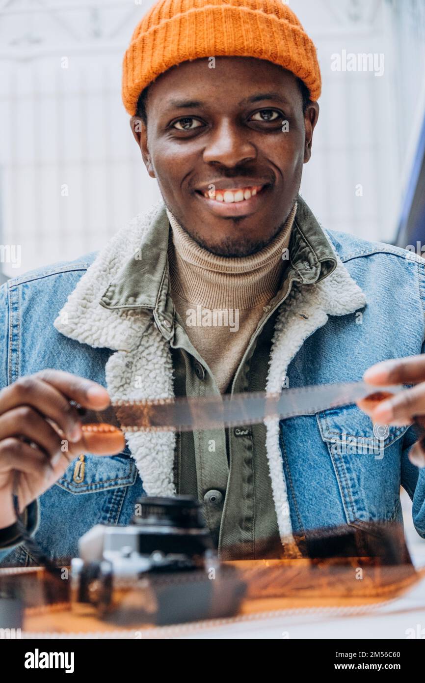 L'homme afro-américain séduisant en veste denim et chapeau orange tient le film vintage à la table dans la salle lumineuse de très gros plan Banque D'Images