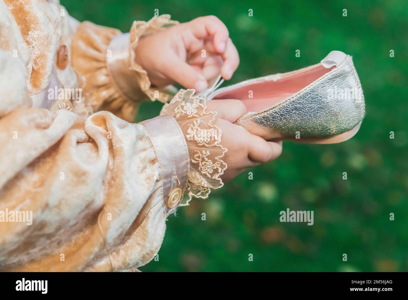 bébé en costume de princesse tenant de petites chaussures dorées dans les mains Banque D'Images