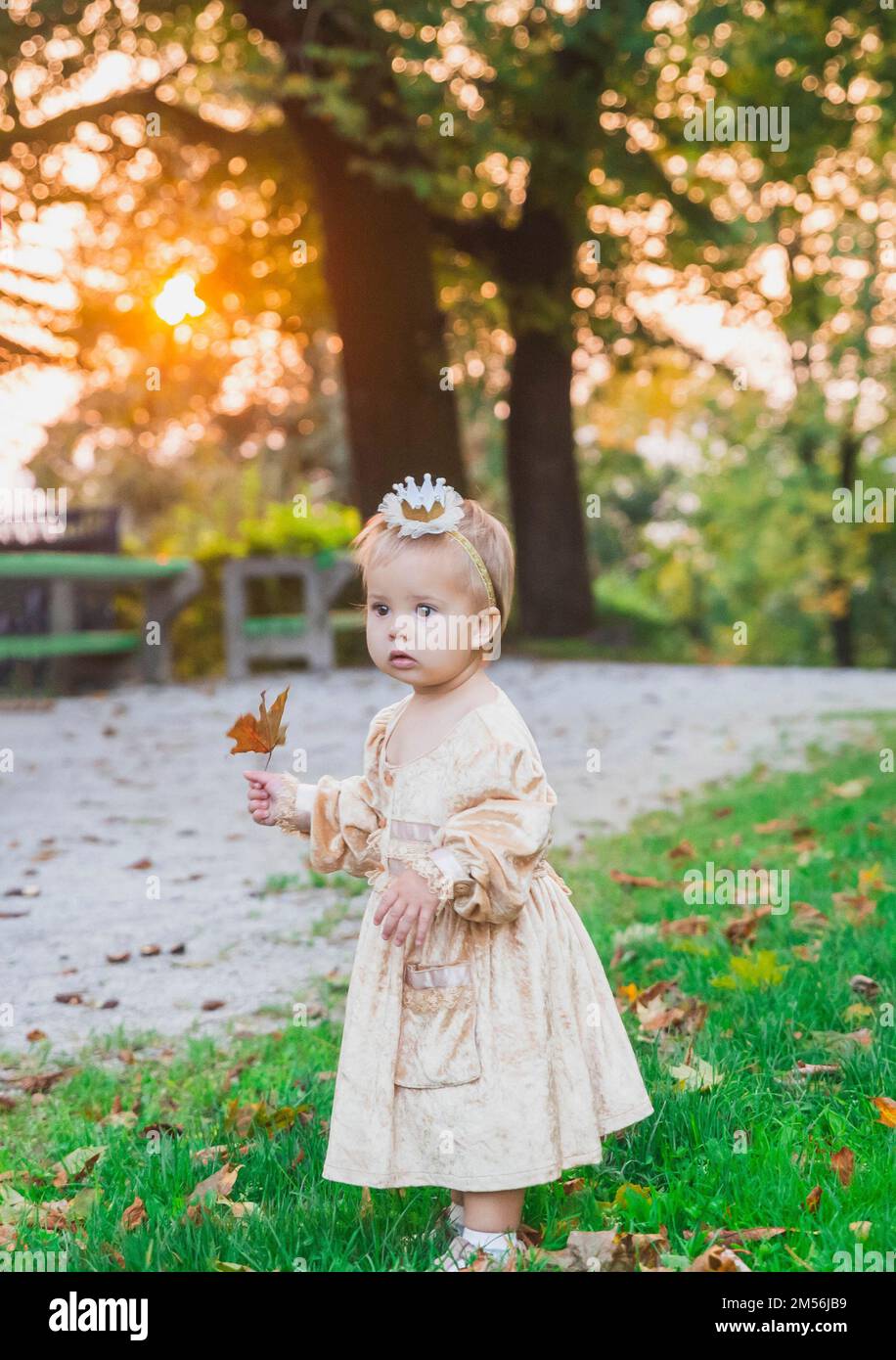 bébé charmant en costume de princesse marche dans le parc au coucher du soleil Banque D'Images