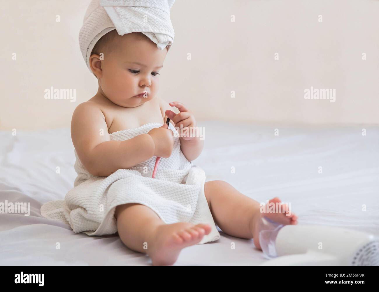 beau bébé avec une serviette sur sa tête regarde l'eyeliner pour les paupières Banque D'Images