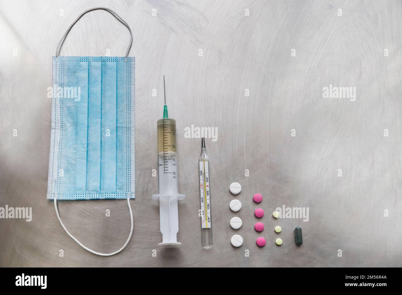 masque de protection, seringue, thermomètre et pilules sur table médicale métallique Banque D'Images