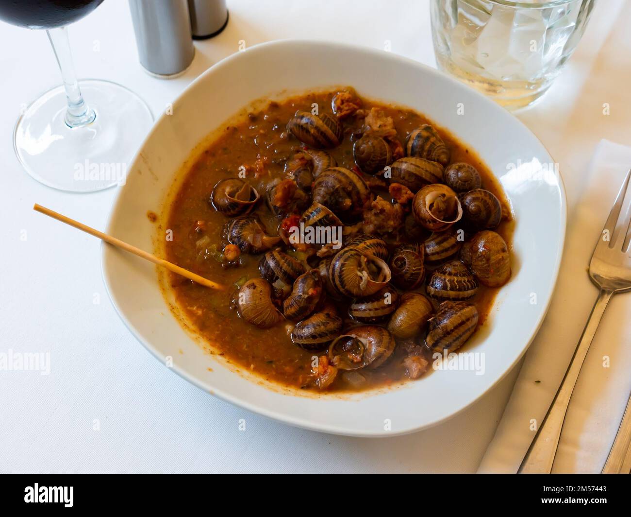 Des escargots compotés dans de la sauce rouge servis sur une assiette en céramique blanche près des couverts et du pain dans le restaurant Banque D'Images