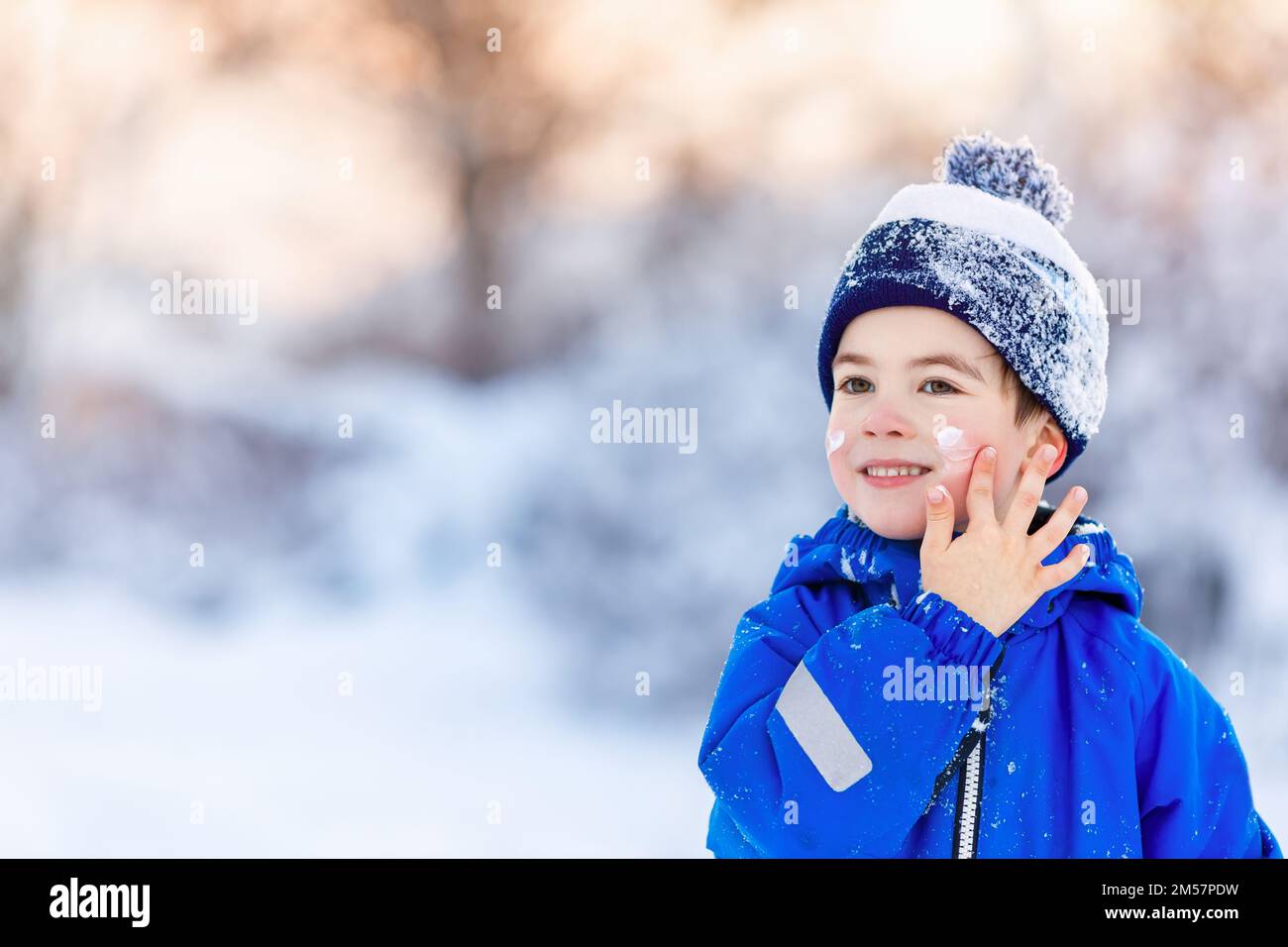 portrait d'un petit garçon souriant appliquant de la crème froide sur le visage Banque D'Images