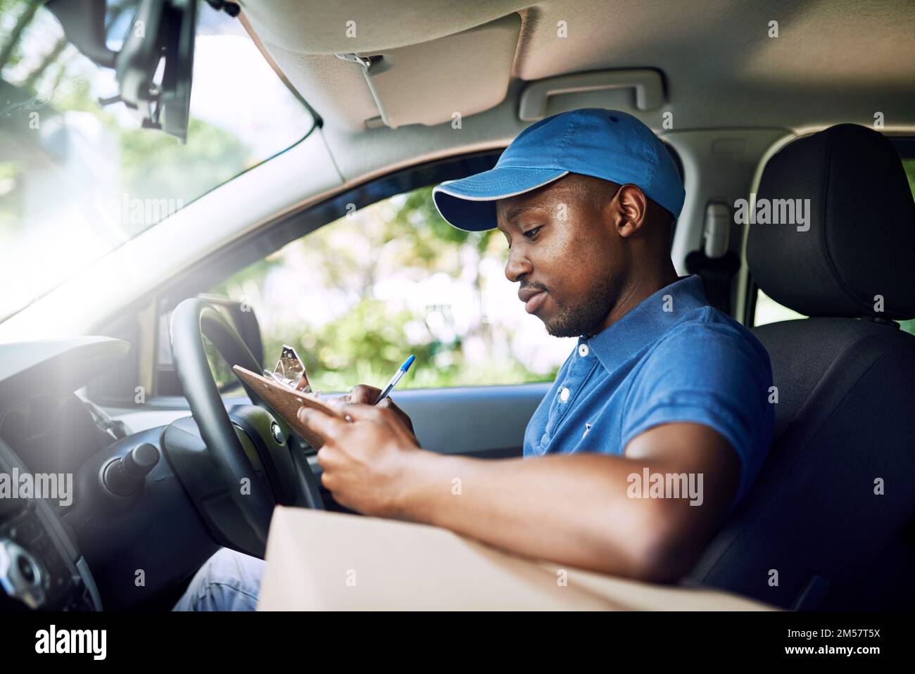 Enregistrer chacune de ses livraisons. un jeune poste travaillant assis dans sa voiture pendant une livraison. Banque D'Images