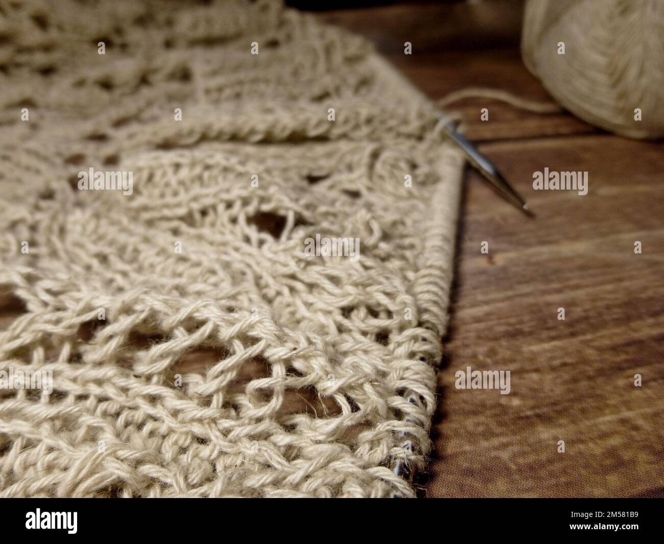 Nappe ajourée dans le processus de tricotage. Aiguilles à tricoter, boucles sur aiguilles à tricoter, tissu tricoté, pelote de fil, coton grossier et lin Banque D'Images