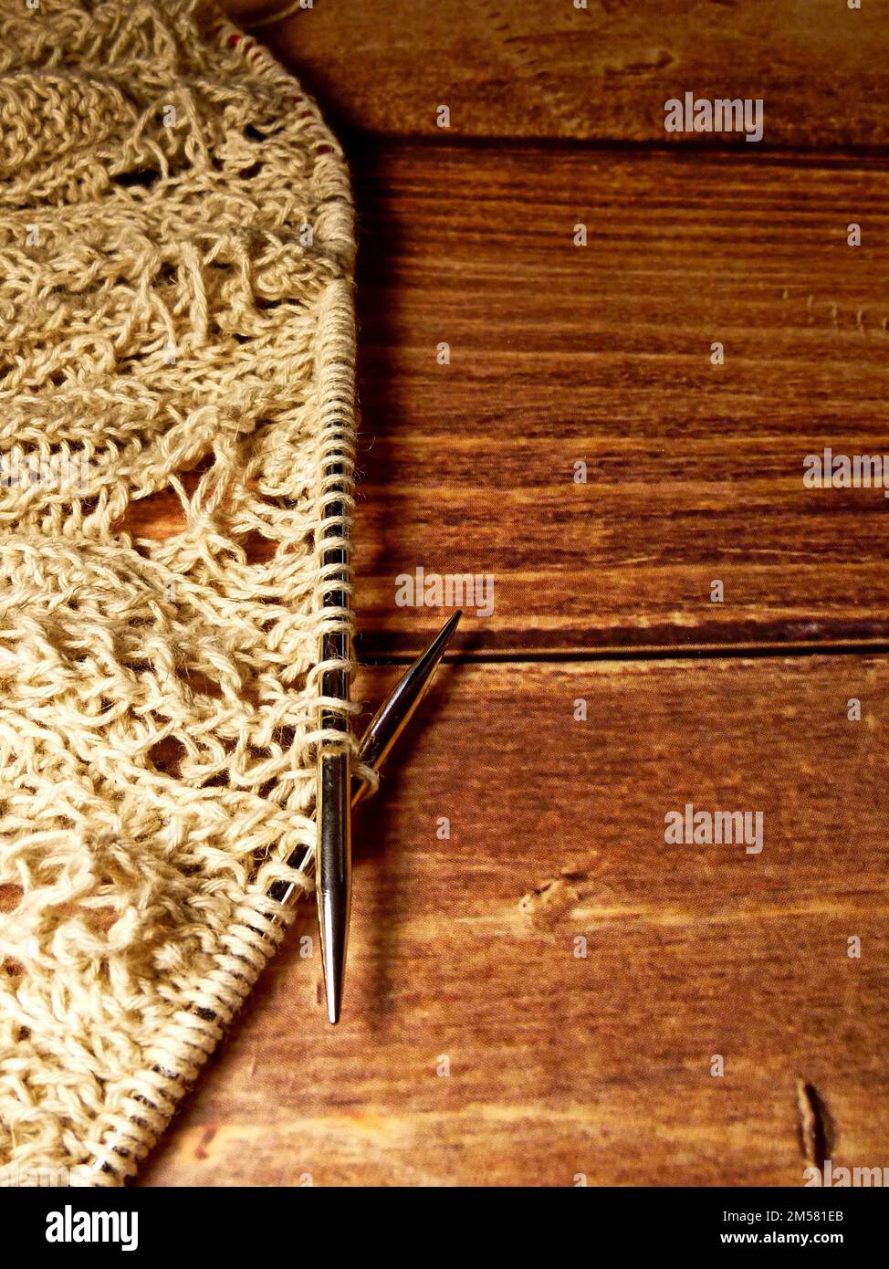 Nappe ajourée dans le processus de tricotage. Aiguilles à tricoter, boucles sur aiguilles à tricoter, tissu tricoté, coton grossier et fil de lin, dos en bois Banque D'Images