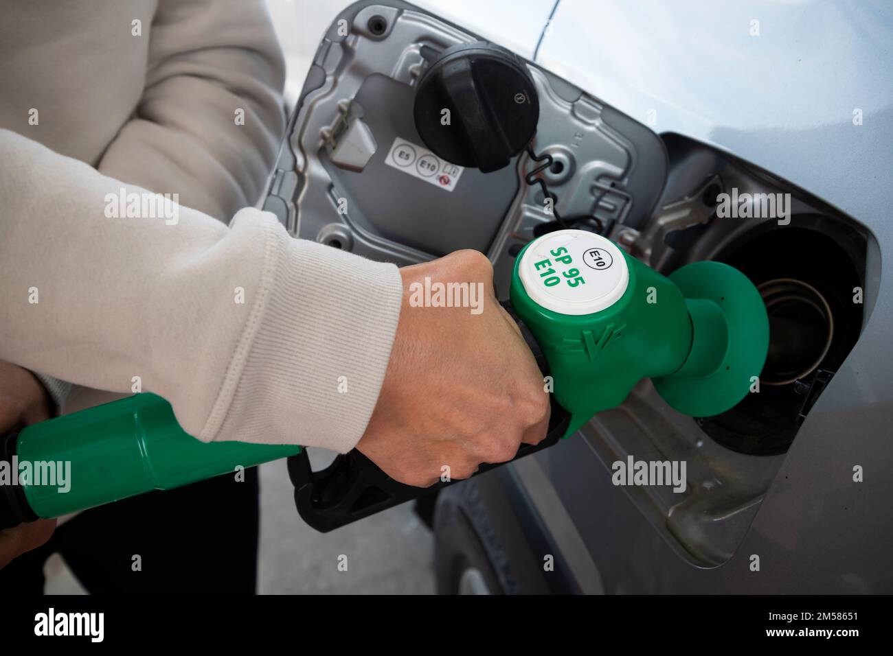Femme attrapant la buse de carburant verte dans une main tout en remplissant SP95 E10 essence de sa voiture dans la station-service en France Banque D'Images