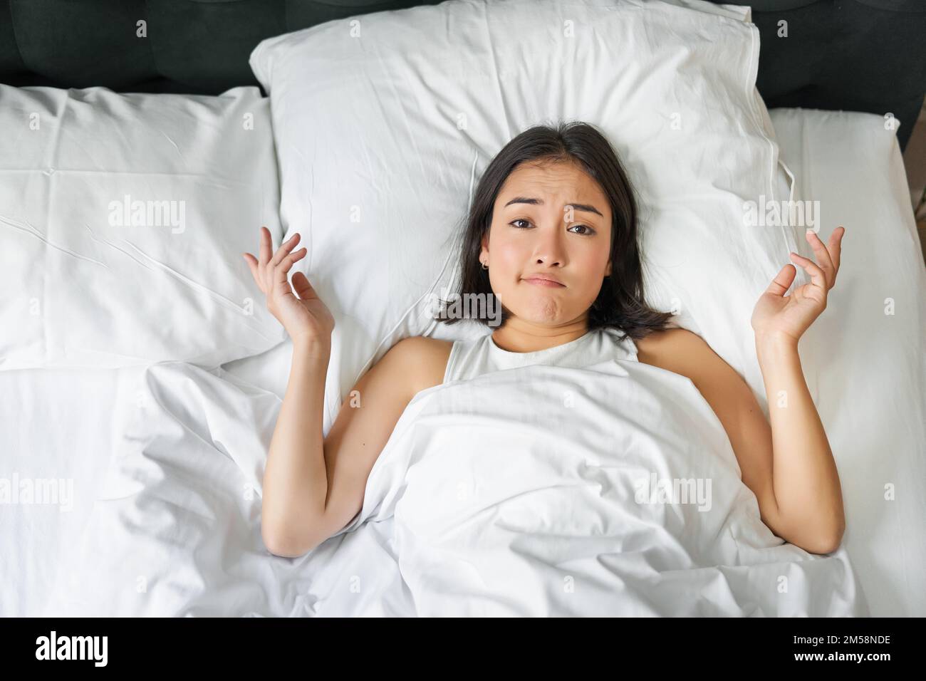 Portrait d'une fille asiatique couchée dans son lit et ses haussoles,  semble perplexe, trop de réflexion avant d'aller dormir, regardant  compliqué à la caméra Photo Stock - Alamy