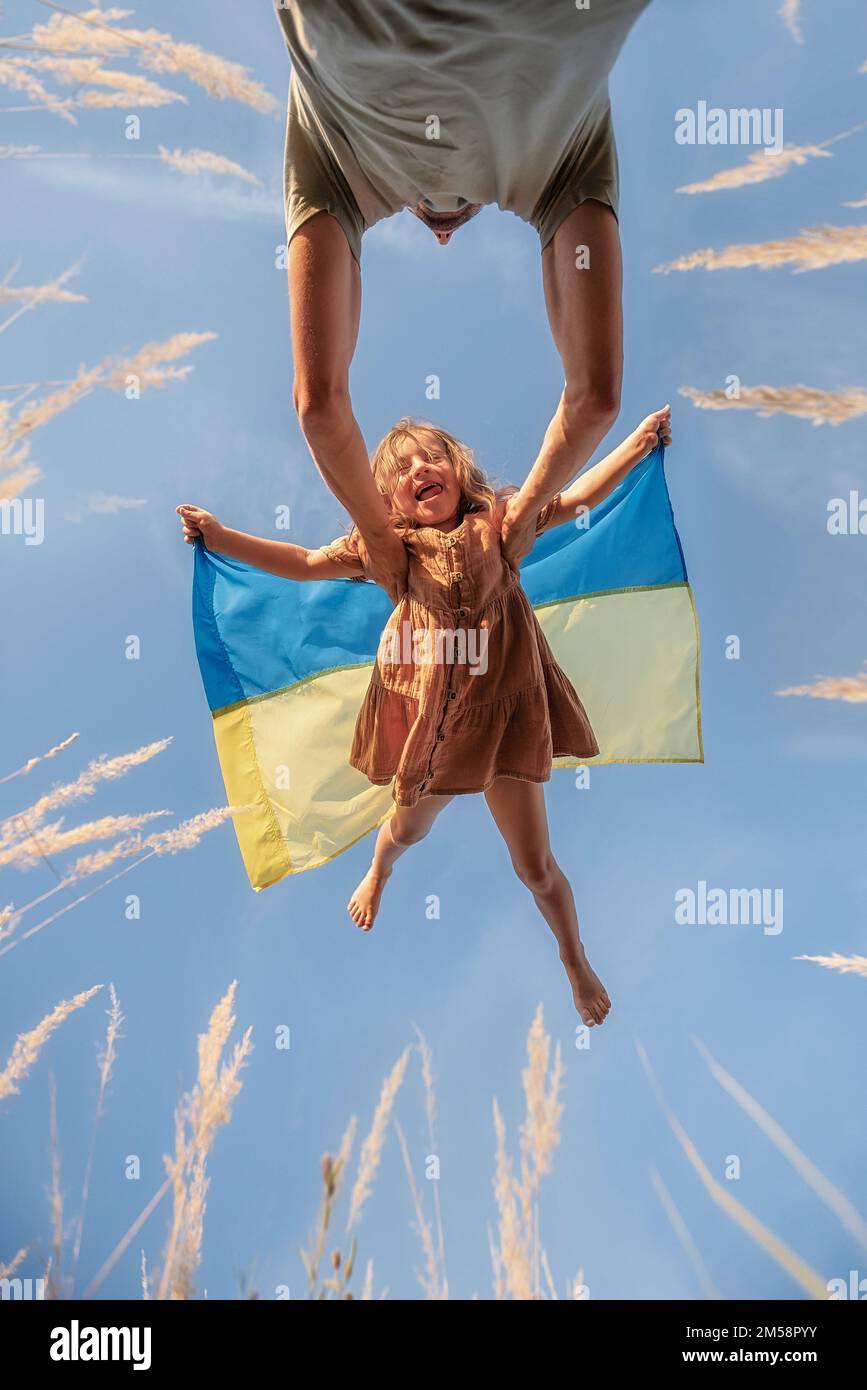 L'homme jette une petite fille qui tient le drapeau bleu jaune de l'Ukraine dans les mains contre fond ciel clair. La rencontre tant attendue du père et de la fille Banque D'Images