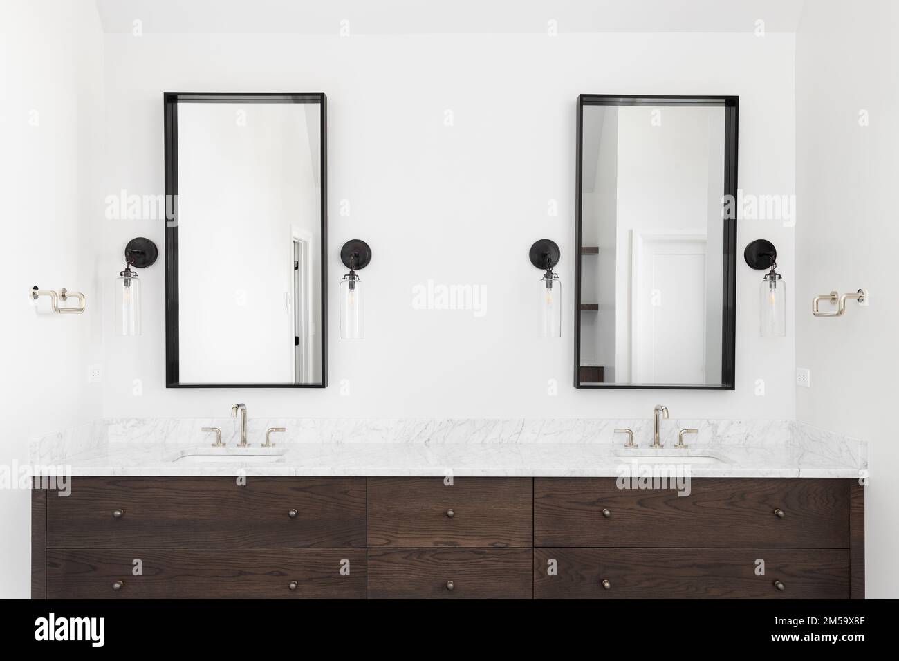 Une salle de bains de luxe avec une armoire en bois sombre, un comptoir en marbre et des lumières de conce autour des miroirs carrés. Banque D'Images