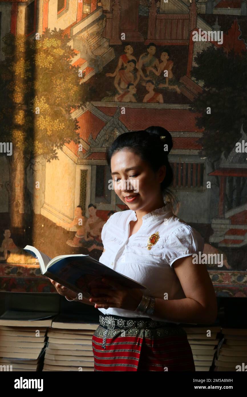 Femme thaïlandaise en costume thaïlandais lire le livre dans le fond de peinture thaï Banque D'Images