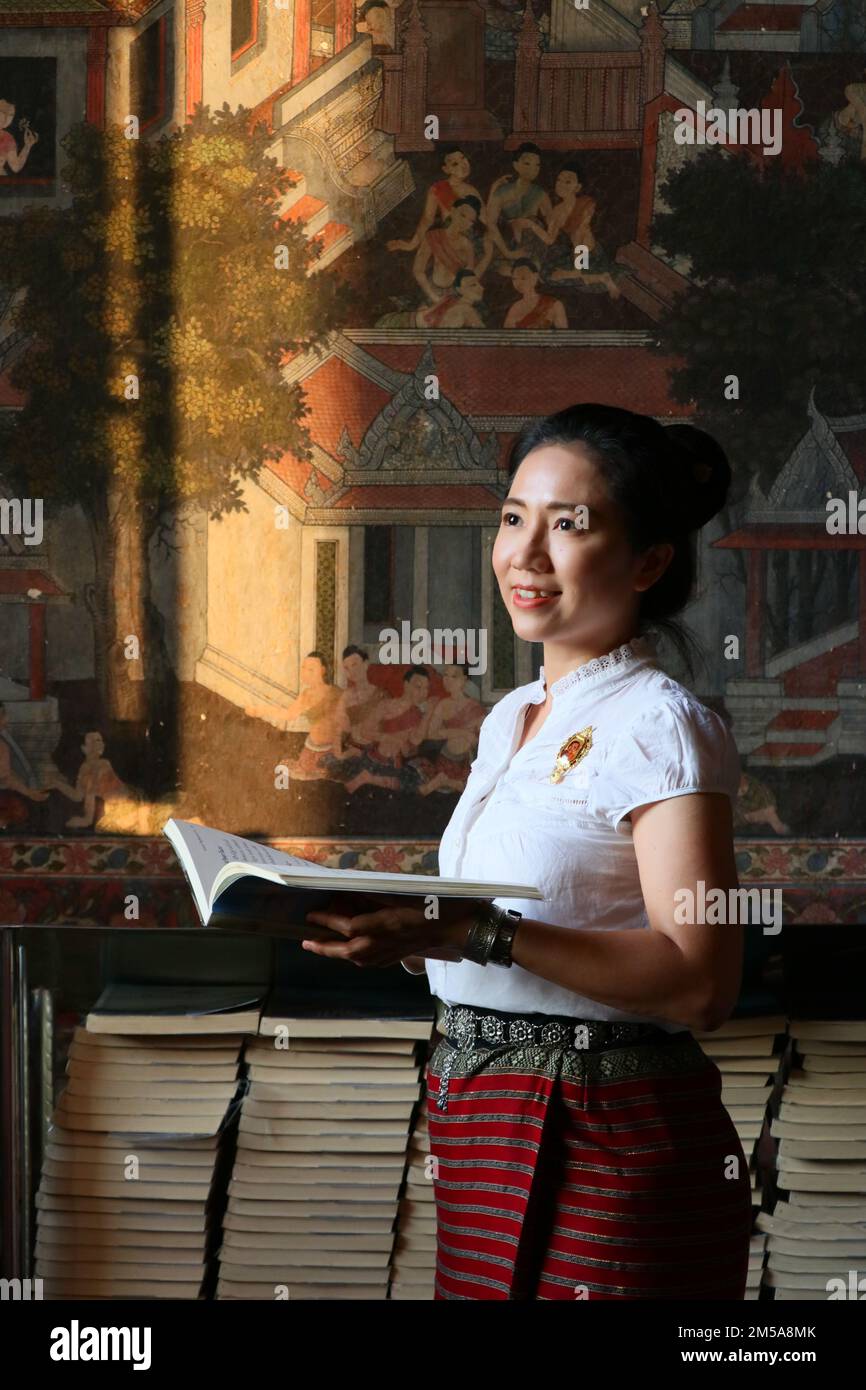Femme thaïlandaise en costume thaïlandais lire le livre dans le fond de peinture thaï Banque D'Images