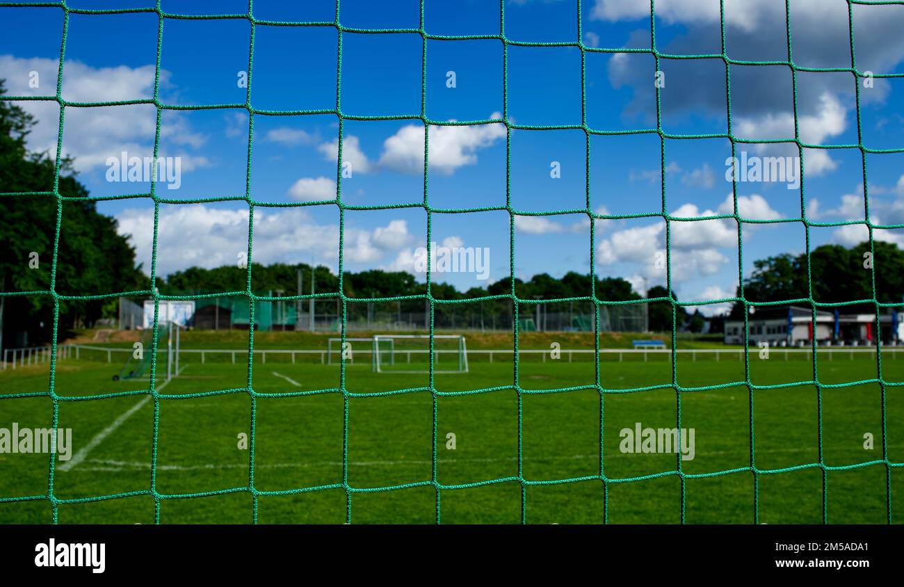 Vue à travers un filet de but de football sur un terrain de sport déserté avec pelouse verte fraîche et ciel bleu (variante A) Banque D'Images