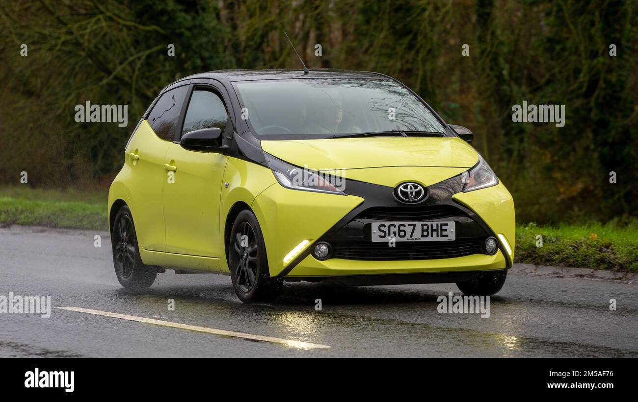 2017 voiture jaune Toyota Aygo conduite sur route mouillée avec phares allumés Banque D'Images