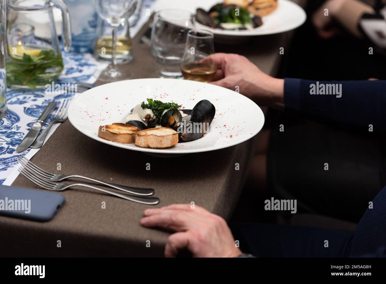 homme qui va manger des moules dans une sauce au vin blanc et des toasts de pain blanc dans un restaurant Banque D'Images