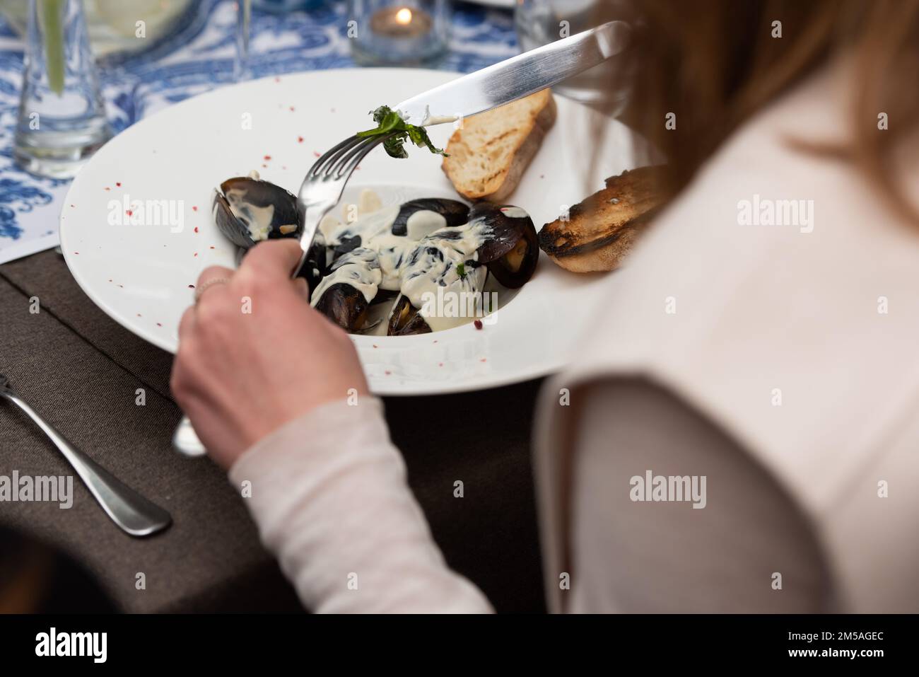 femme qui va manger des moules dans une sauce au vin blanc et des toasts de pain blanc dans un restaurant Banque D'Images