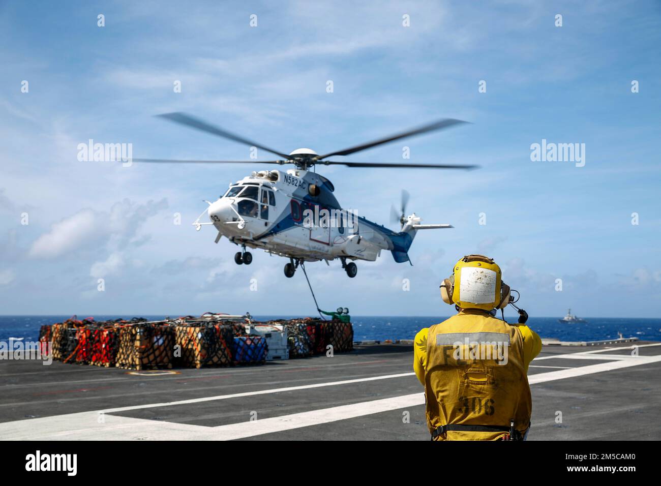 MER DES PHILIPPINES (1 mars 2022) Aviation Boatswain's Mate (Handling) 2nd classe Alasdair Reid, de Wellington, Nouvelle-Zélande, dirige un Super Puma AS332 sur le pont de vol du porte-avions de la classe Nimitz Abraham USS Lincoln (CVN 72) Lors d'un réapprovisionnement en mer avec le navire de fret sec et de munitions du Commandement du Seallift militaire USNS Matthew Perry (T-AKE 9). Abraham Lincoln Strike Group est en cours de déploiement prévu dans la zone d'exploitation de la flotte américaine 7th afin d'améliorer l'interopérabilité par le biais d'alliances et de partenariats tout en servant de force de réaction prête à l'emploi pour soutenir un Indo-PAC libre et ouvert Banque D'Images