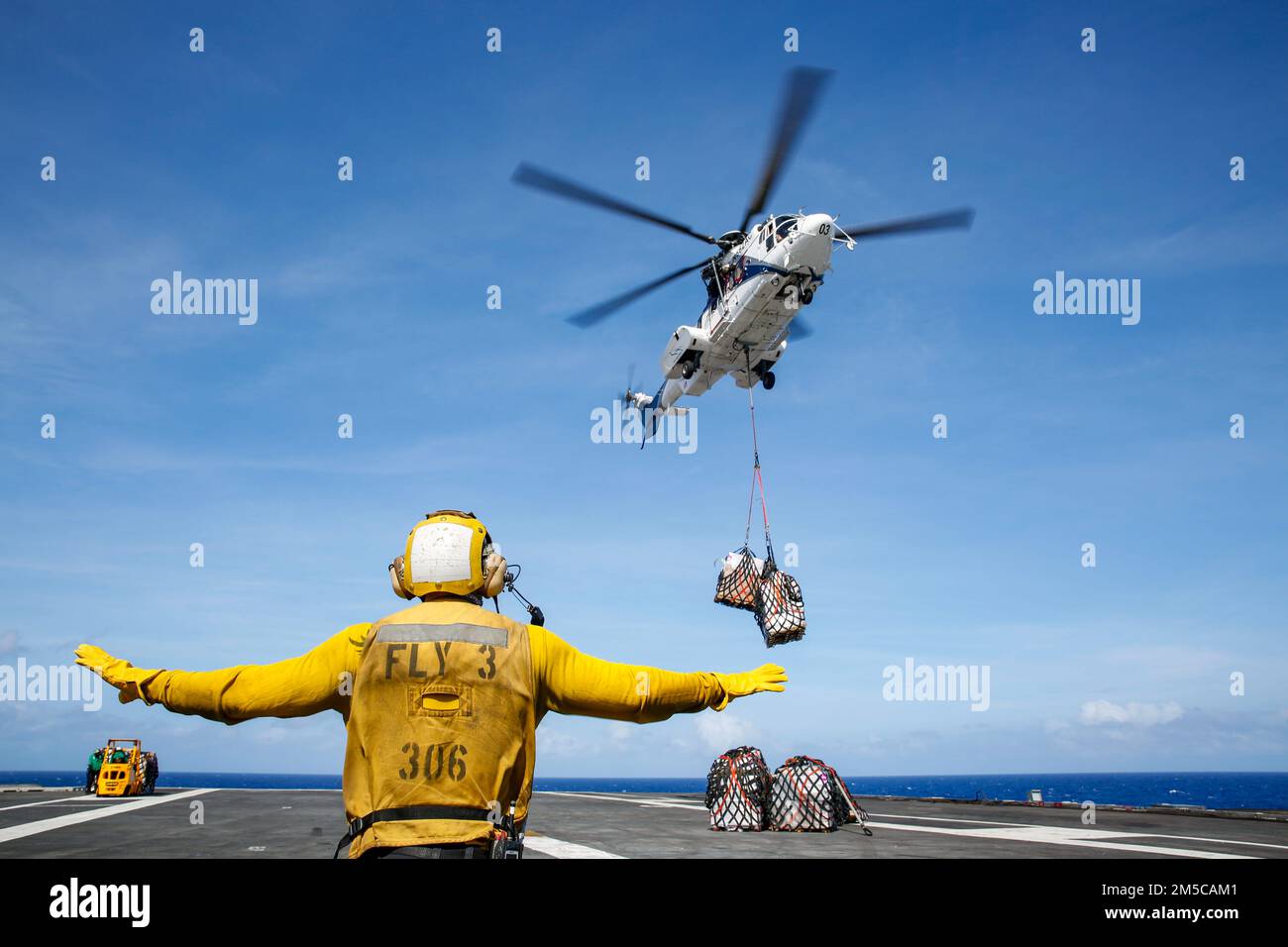 MER DES PHILIPPINES (1 mars 2022) Aviation Boatswain's Mate (Handling) 2nd classe Alasdair Reid, de Wellington, Nouvelle-Zélande, dirige un Super Puma AS332 sur le pont de vol du porte-avions de la classe Nimitz Abraham USS Lincoln (CVN 72) Lors d'un réapprovisionnement en mer avec le navire de fret sec et de munitions du Commandement du Seallift militaire USNS Matthew Perry (T-AKE 9). Abraham Lincoln Strike Group est en cours de déploiement prévu dans la zone d'exploitation de la flotte américaine 7th afin d'améliorer l'interopérabilité par le biais d'alliances et de partenariats tout en servant de force de réaction prête à l'emploi pour soutenir un Indo-PAC libre et ouvert Banque D'Images