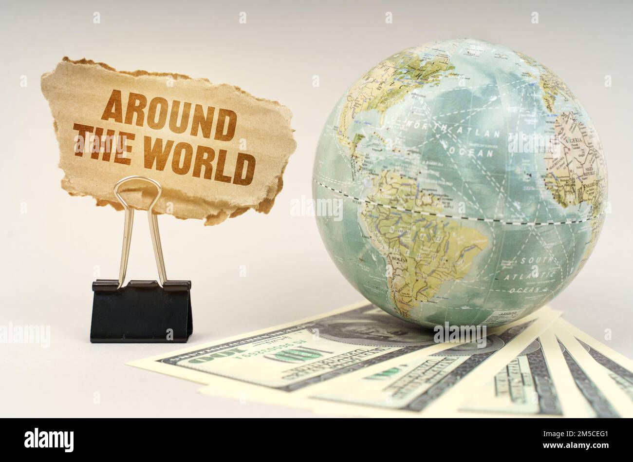 Concept d'entreprise. Sur une surface grise, un globe, des dollars et une plaque de carton avec inscription - autour du monde Banque D'Images