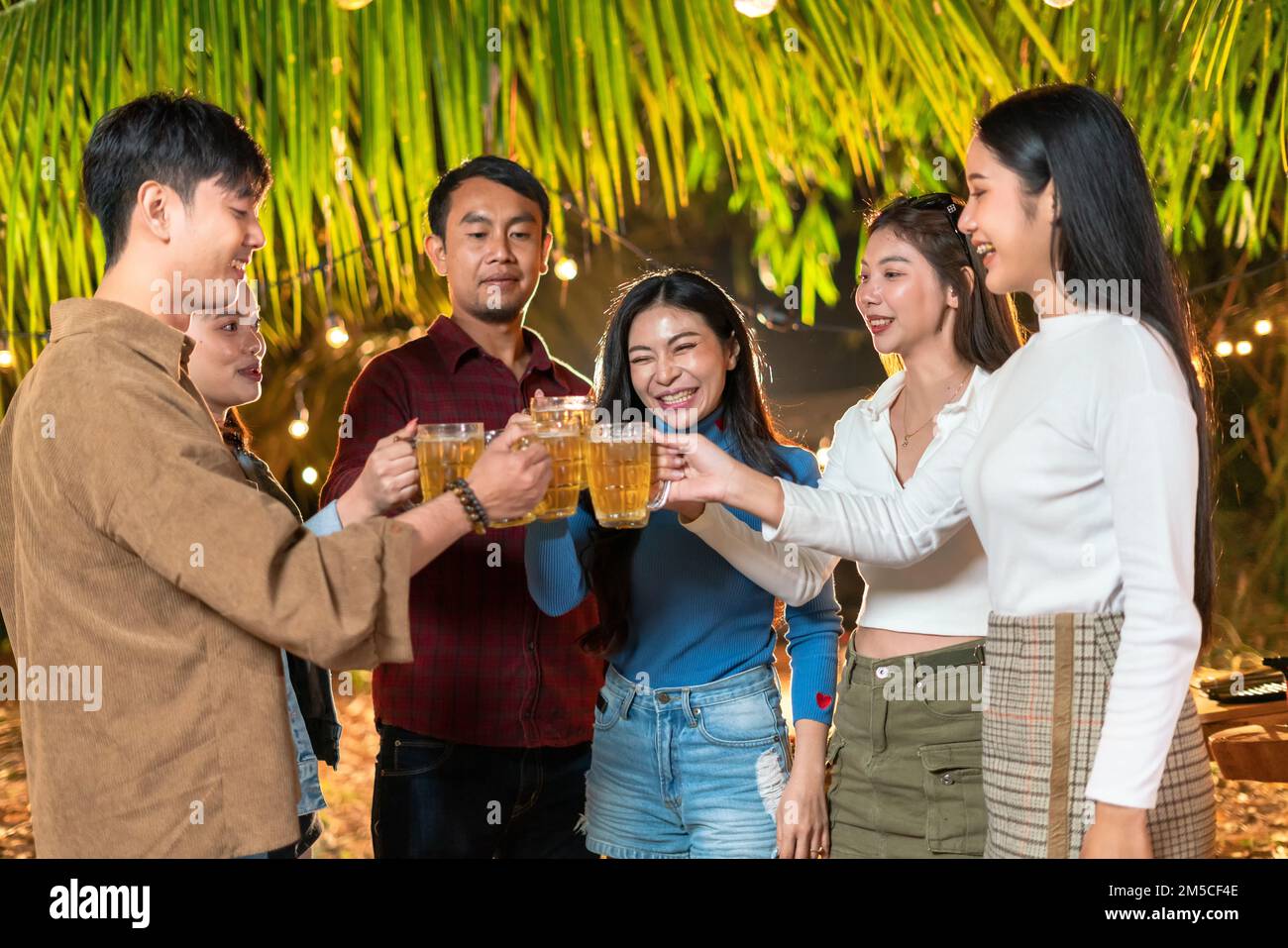 Un groupe d'amis se réjouisse de se tenir debout et de griller des bières à la fête. Banque D'Images
