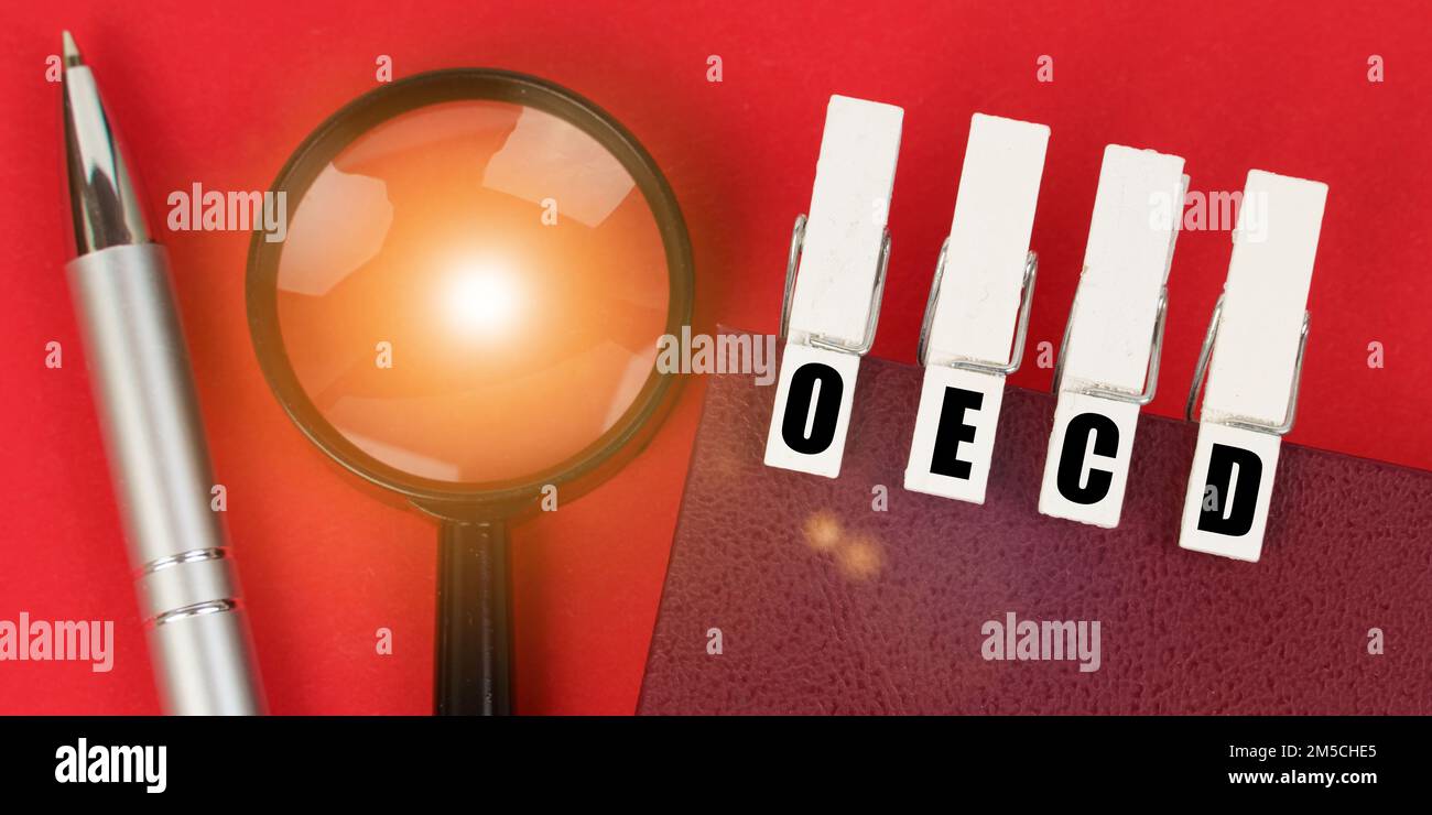 Concept d'entreprise. Sur la surface rouge, il y a une loupe, un bloc-notes et des épingles à linge avec l'inscription OCDE Banque D'Images