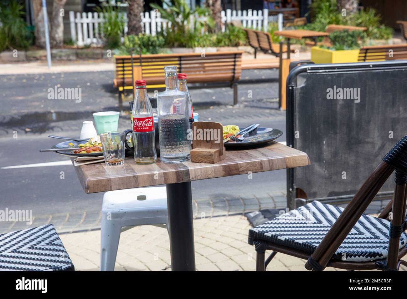 Table de petit-déjeuner dans un café à Avalon Beach Sydney avec les restes de nourriture, bouteille de coca vide et tasses de café, NSW, Australie Banque D'Images