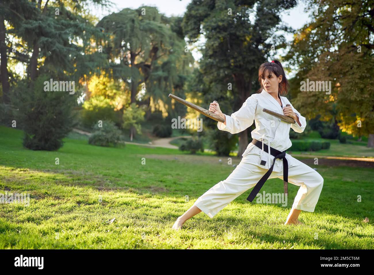 Carate chasseur femme dans un kimono blanc et ceinture noire dans la position de combat à l'extérieur dans la nature. Sports et arts martiaux concept. Banque D'Images
