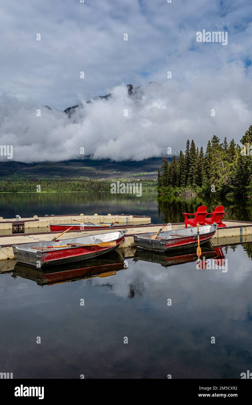 Des nuages bas un matin encore au lac Pyramid, quai du parc national Jasper avec des bateaux et des chaises rouges Banque D'Images
