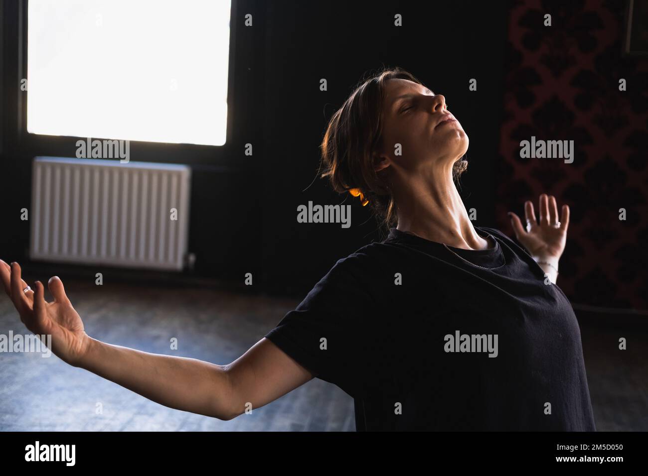 Une yogi femme faisant une posture de rembpoint avec les bras ouverts pendant son entraînement de yoga de flux vinyasa à côté d'une fenêtre avec belle lumière intense Banque D'Images