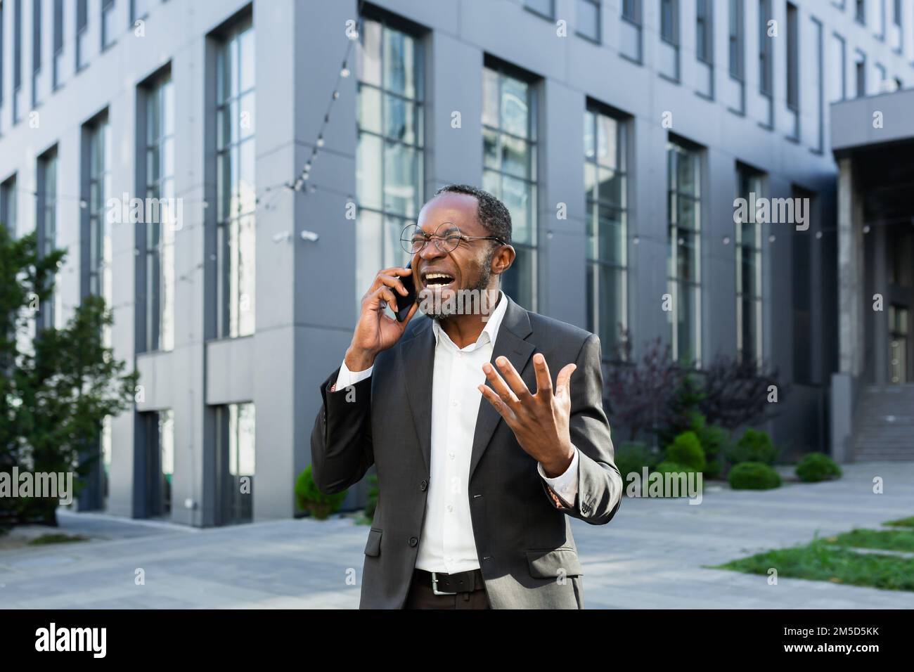 Un patron afro-américain en colère se disputant et criant en parlant au téléphone, un homme d'affaires en costume devant l'immeuble de bureaux. Banque D'Images