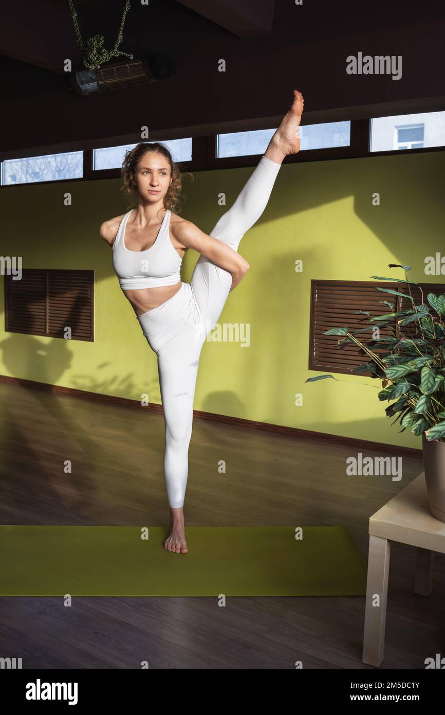Jeune femme athlétique pratiquant le yoga, faisant une variation de l'exercice Trivikramasana, debout avec sa jambe étendue, s'exerçant seul dans le cracher blanc Banque D'Images