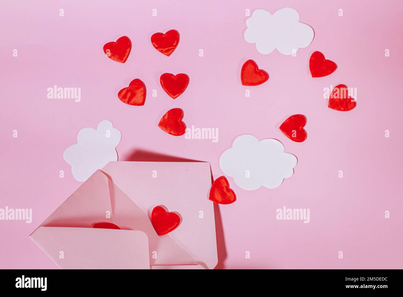Une enveloppe postale ouverte avec des coeurs rouges et des nuages qui en sortent. Les cœurs volent hors d'une enveloppe d'artisanat ouverte. Le papier s'assombrit sur un fond rose Banque D'Images