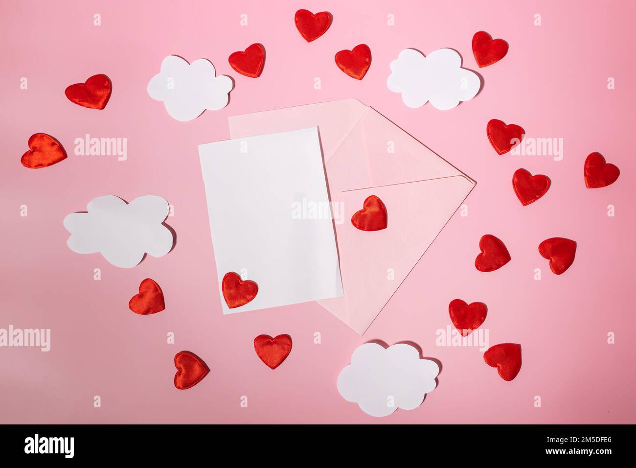 Une enveloppe postale ouverte avec des coeurs rouges et des nuages qui en sortent. Les cœurs volent hors d'une enveloppe d'artisanat ouverte. Le papier s'assombrit sur un fond rose Banque D'Images