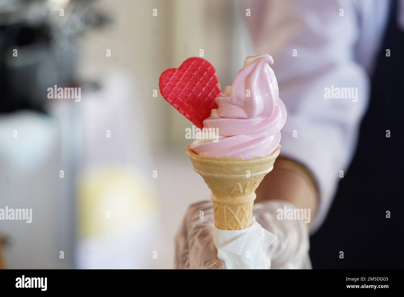Un ouvrier avec des gants tenant un cône de crème glacée avec un mélange de saveurs rose et vanille. Glace rose à coeur rouge. Banque D'Images