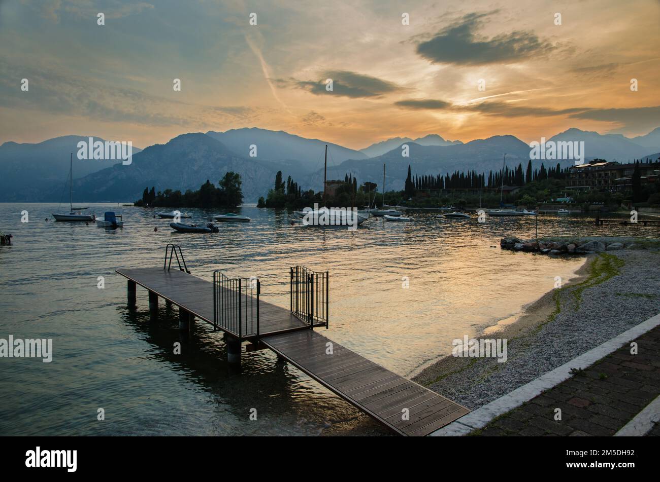 Bateaux amarrés et une petite jetée sur le lac de Garde au coucher du soleil, Malcesine, Italie Banque D'Images