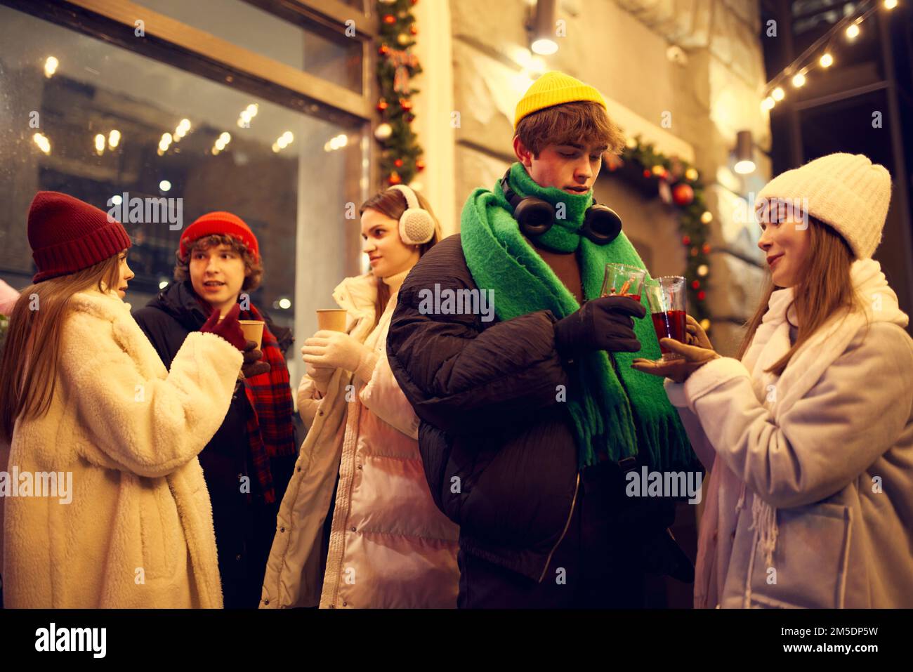 Groupe de jeunes, garçons et filles qui passent du temps ensemble dans une rue de Noël festive, goûtant du vin chaud et du café. Concept de l'hiver Banque D'Images