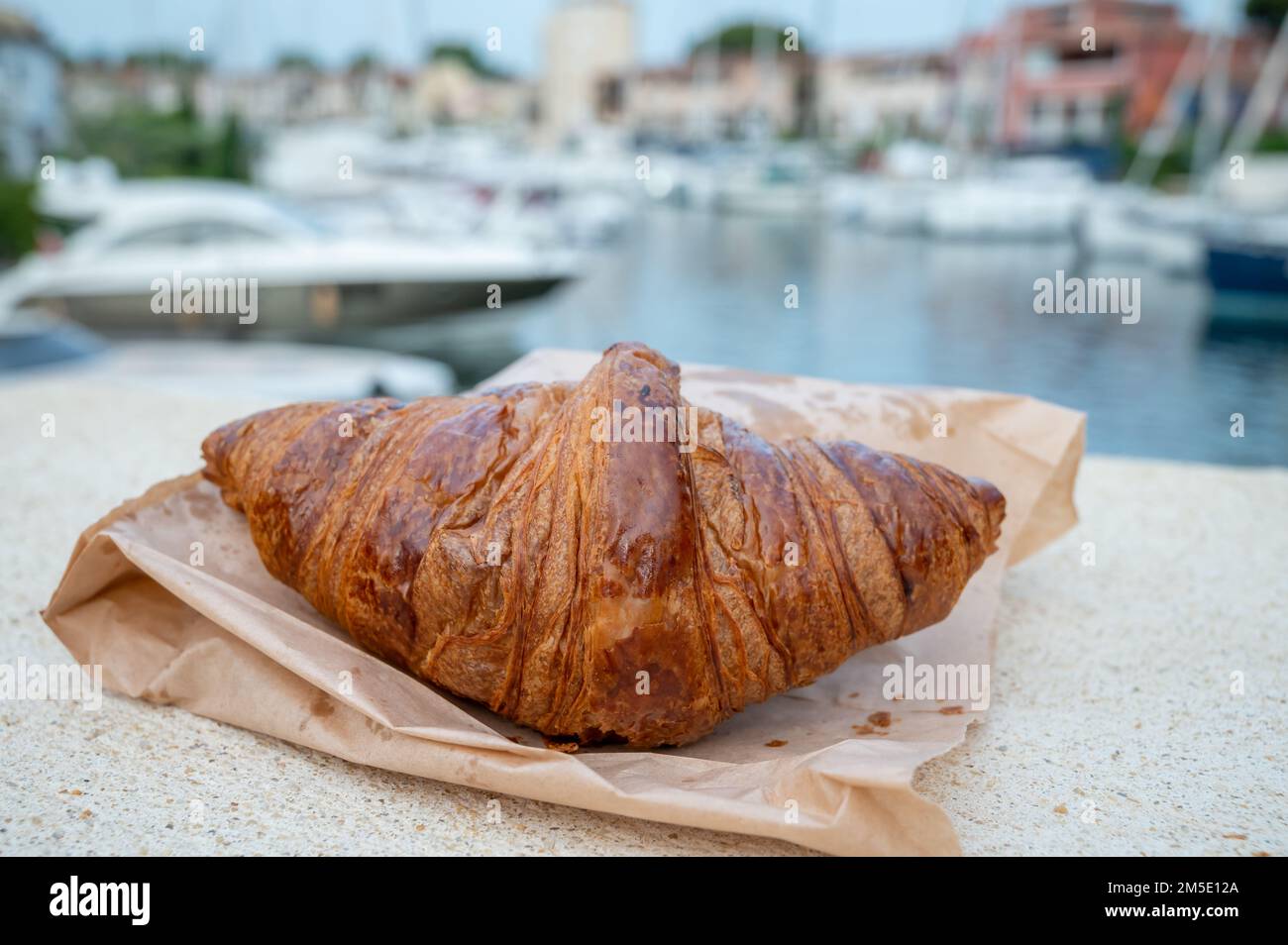 Croissant français frais et bateaux de Port Grimaud en arrière-plan, style de vie dans le sud de la France Banque D'Images