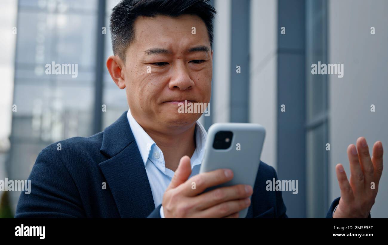 Triste asiatique d'âge moyen homme d'affaires fou malheureux homme d'affaires se sentant ennuyé avec l'utilisation cassé de smartphone problème de batterie faible en colère d'avoir le problème avec Banque D'Images