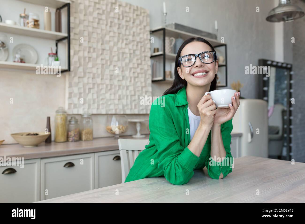 Jeune belle femme, mère boit du café, du thé seul dans la cuisine à la maison. Il tient une tasse dans ses mains, aime, se repose, sourit à la caméra. Banque D'Images