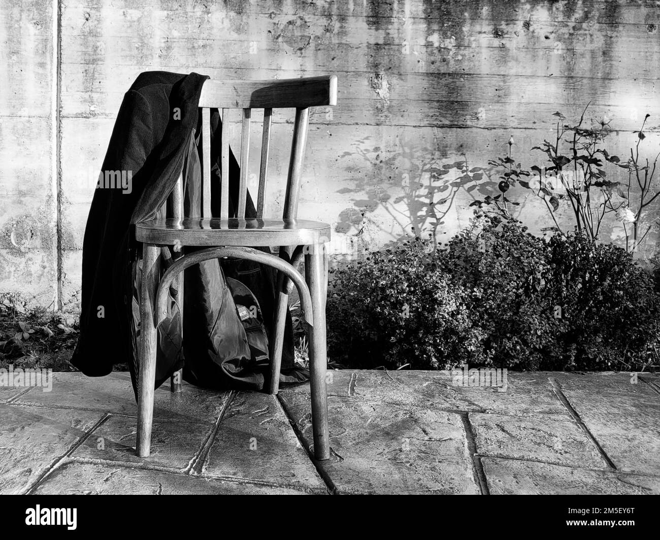 Une photo sombre d'une ancienne chaise en bois dans la cour d'une maison avec une veste noire Banque D'Images