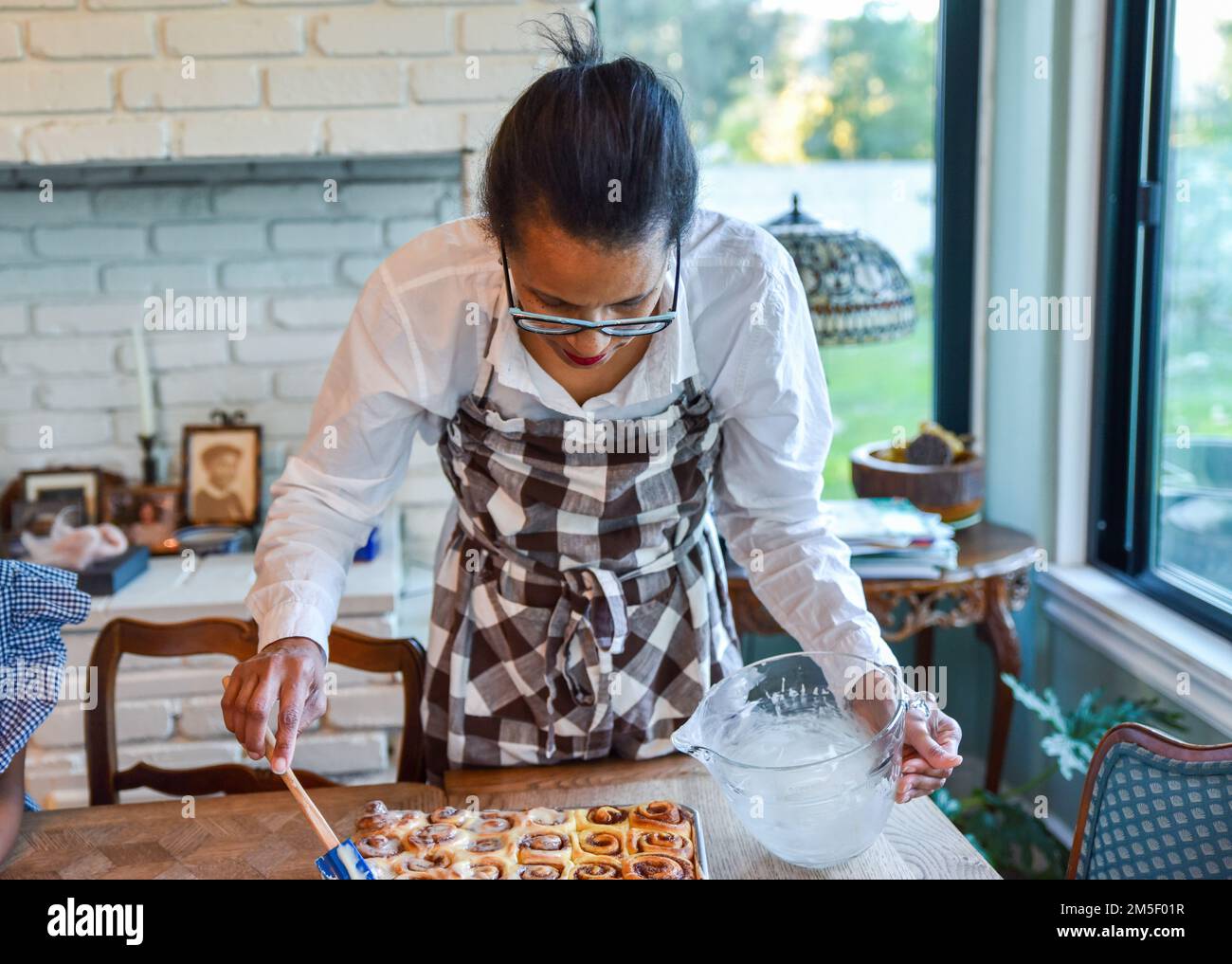 une femme qui pose une grande feuille de petits pains à la cannelle fraîchement cuits place soigneusement dans les rangées en attendant d'être émaillée de glaçage blanc Banque D'Images