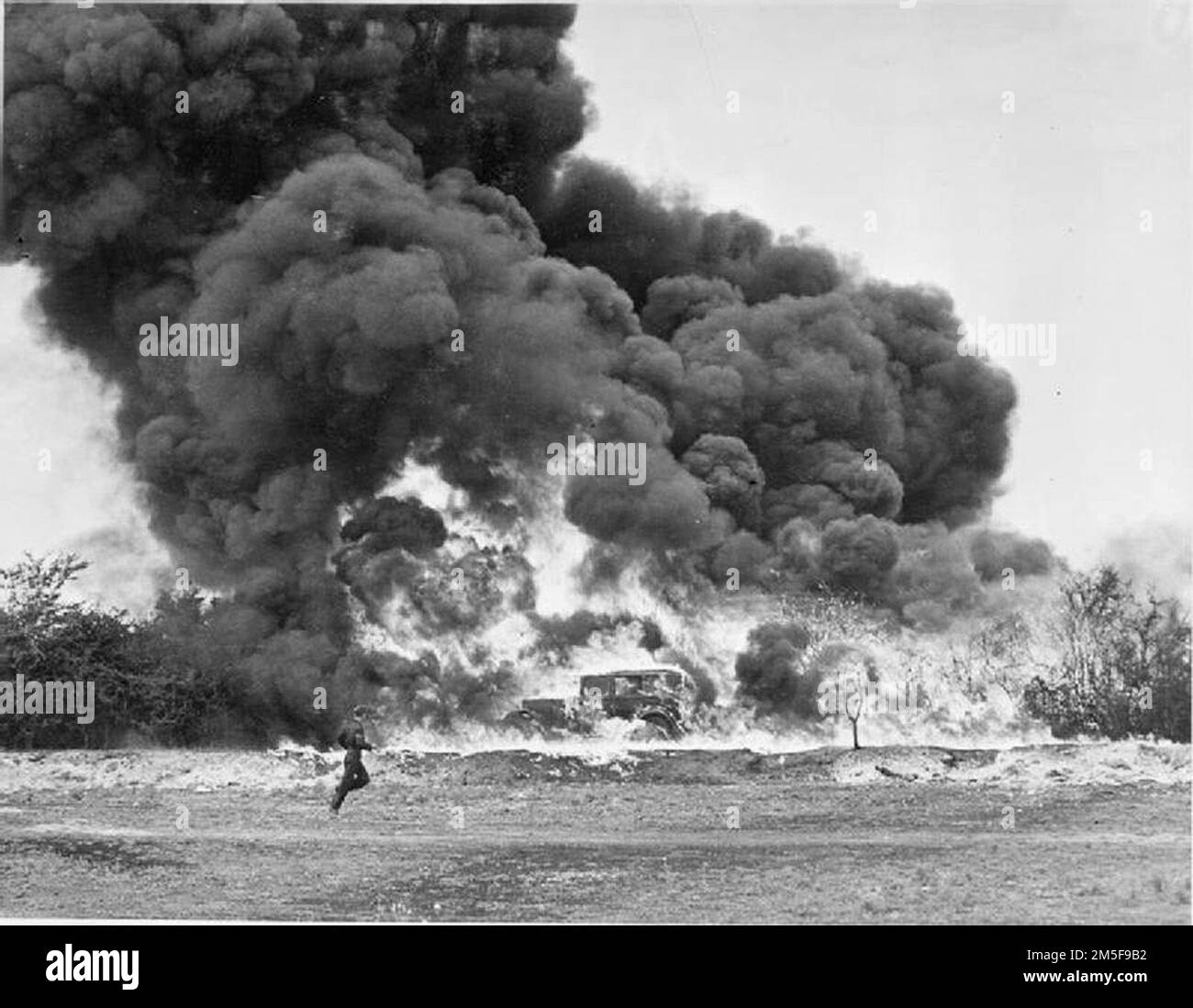 Armes pétrolières contre l'invasion - une démonstration de défenses anti-invasion, Royaume-Uni, 1945 Une démonstration de 'Fougasse', quelque part en Grande-Bretagne. Une voiture est entourée de flammes et d'un énorme nuage de fumée. Au premier plan, on peut voir un soldat courir de gauche à droite. Banque D'Images