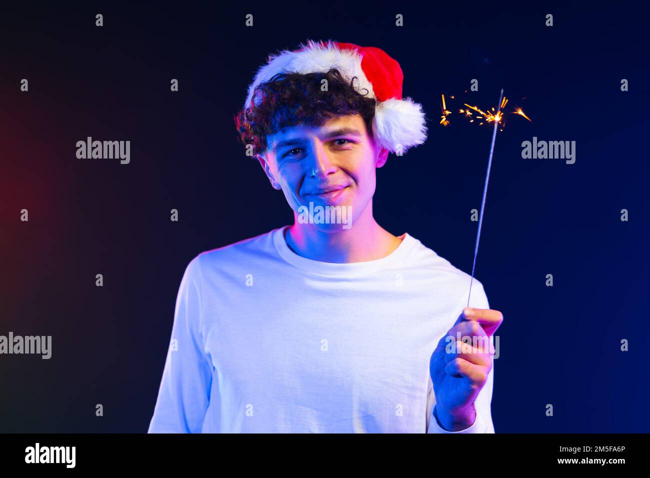 Jeune homme en chapeau de Santa avec le flamant bengale feu sous la lumière du néon. Fête du nouvel an ou de Noël. Un homme joyeux et dynamique. Banque D'Images