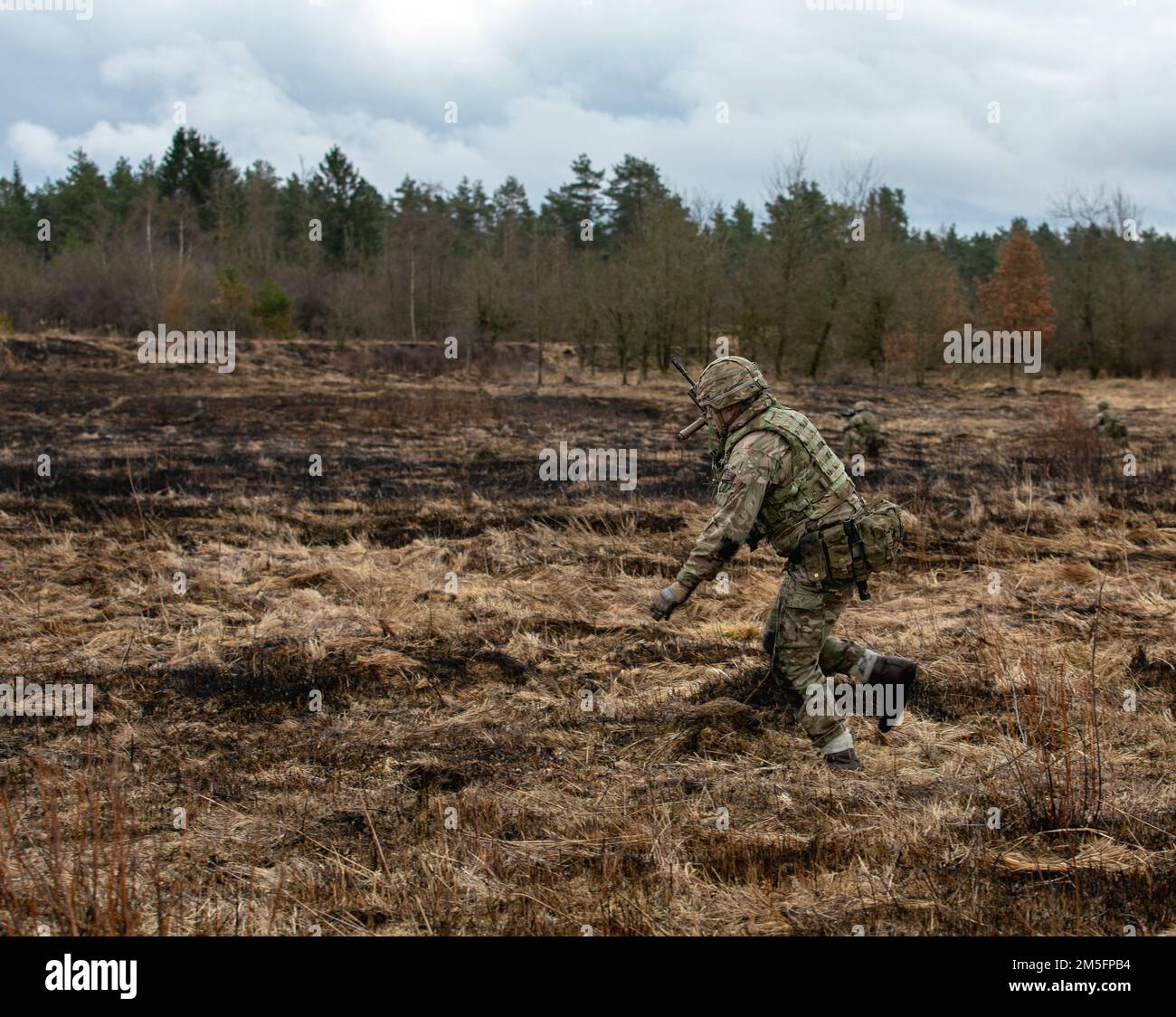 Un officier de l'armée britannique cadet de l'Académie militaire royale Sandhurst assaillit un objectif avec son équipe lors d'un exercice d'entraînement de feu en direct dans la zone d'entraînement de Grafenwoehr du Commandement militaire américain 7th, Grafenwoehr, Allemagne, 14 mars 2022. La formation des cadets de l'officier à Grafenwoehr en est à la première phase de leur mandat senior, la finale de trois de ces termes, et passe pour la première fois par des voies d'entraînement tactique comme celle-ci. Banque D'Images