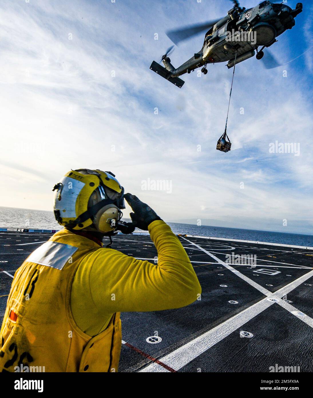 OCÉAN PACIFIQUE (15 mars 2022) Aviation Boatswain’s Mate 3rd classe Kyro Lee, de Miami, affecté au navire de quai de transport amphibie USS John P. Murtha (LPD 26), salue un hélicoptère MH-60s Seahawk attaché aux “Easy Riders” de l’Escadron de frappe maritime d’hélicoptère (HSM) 37 à la suite d’un réapprovisionnement vertical en mer réussi (VERTREP), 15 mars. John P. Murtha mène actuellement des opérations de routine dans la flotte américaine 3rd. Banque D'Images