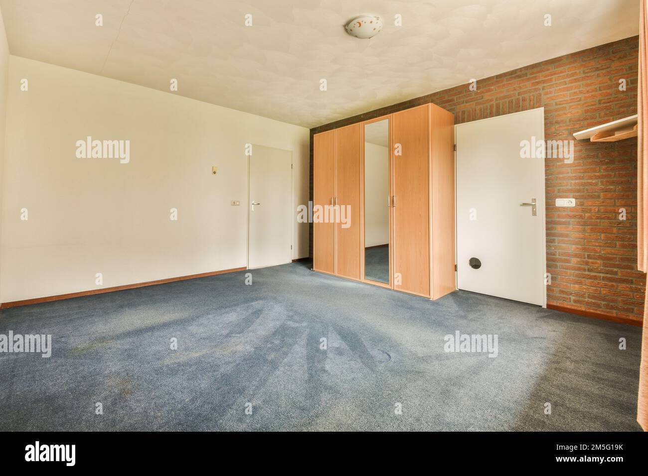 une chambre vide avec moquette bleue et mur de briques rouges en arrière-plan, il y a une porte à une autre pièce Banque D'Images