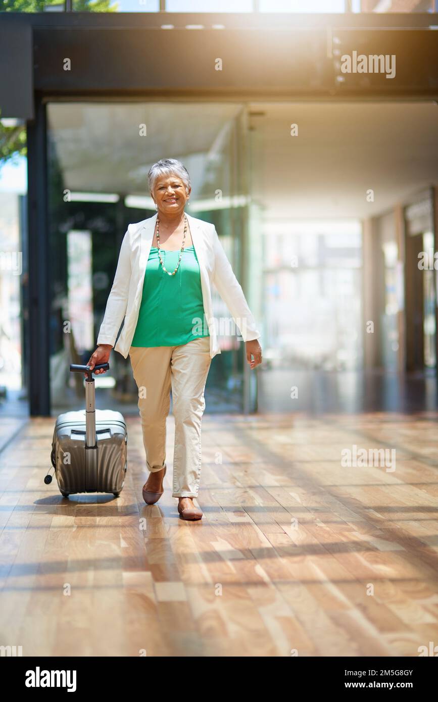 Sur son chemin pour voir le monde. une femme mûre marchant dans un terminal de l'aéroport avec sa valise. Banque D'Images