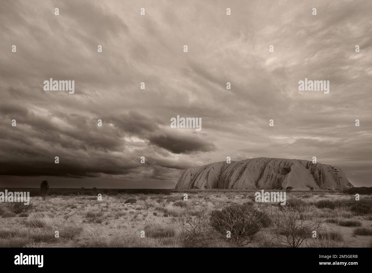 Des nuages de pluie menaçants et sombres s'accrochent au-dessus d'Uluru (Ayers Rock), noir et blanc, sépia, monochrome, Australie Banque D'Images